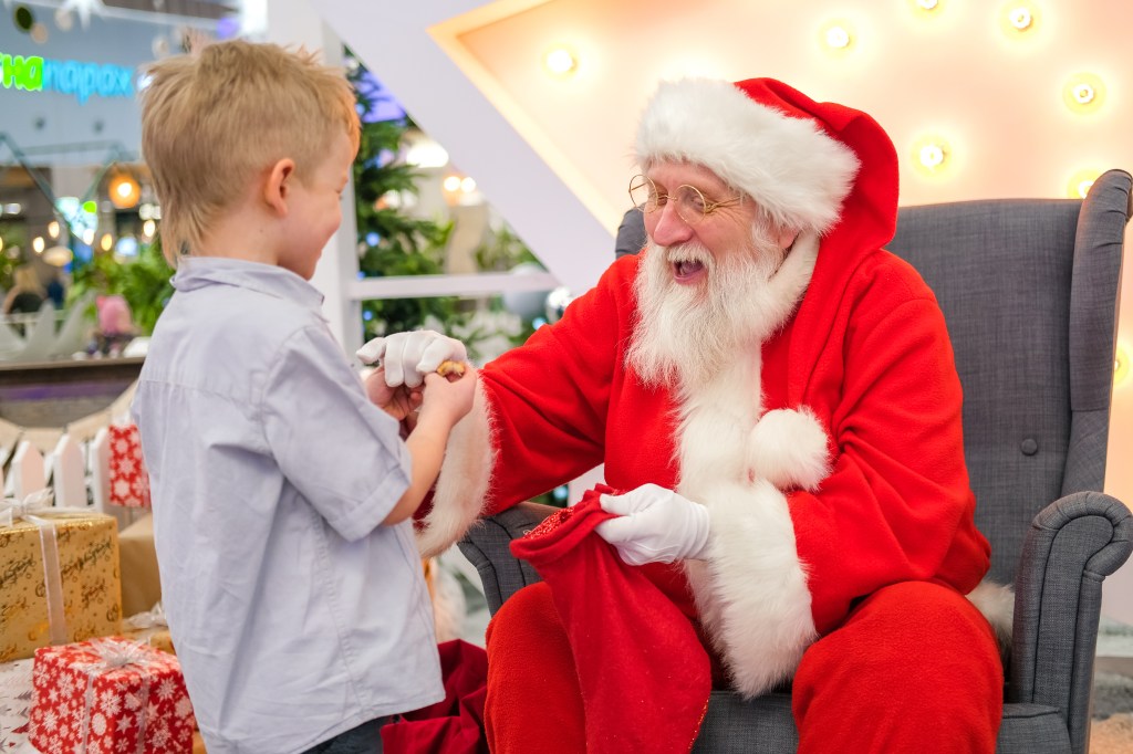 Santa Claus talking and playing surprise games with children in Shopping Mall. Christmas sales and wishes.